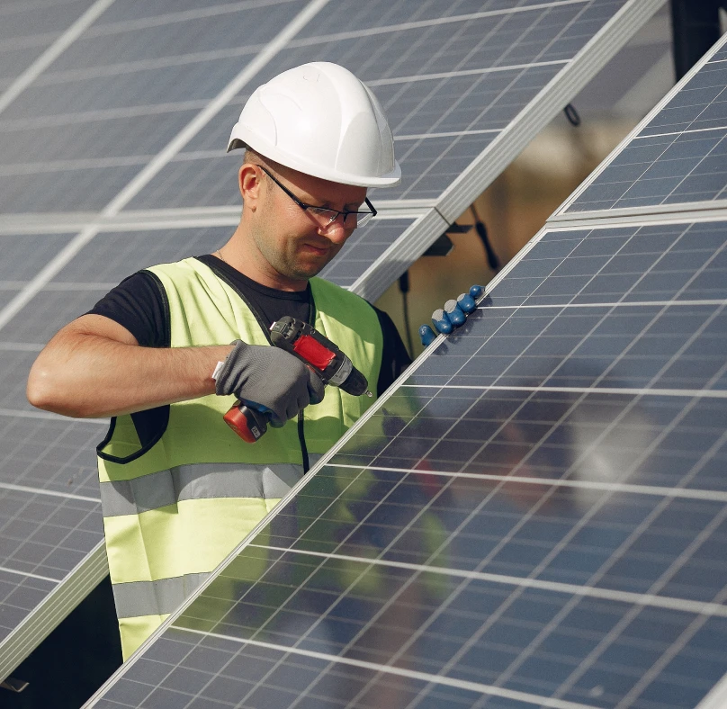 A man in a hard hat and safety vest diligently working on solar panels.